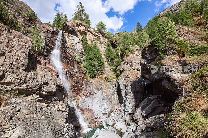 意大利奥斯塔山谷，流动的利拉兹瀑布(Cascate di Lillaz)和花岗岩喀斯特岩石，蓝天白云下的常绿树木